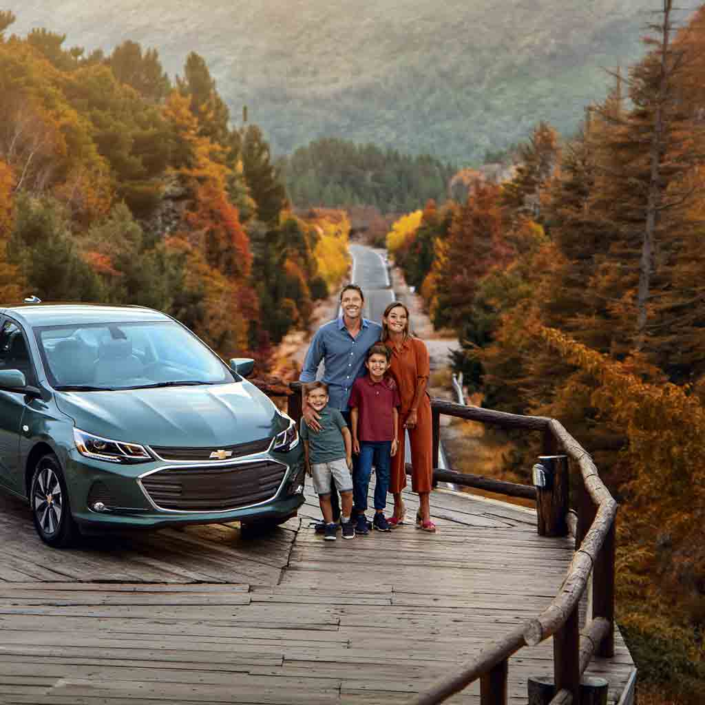 Familia junto a un Chevrolet Onix Sedan de alquiler en la Ruta de los Siete Lagos, San Carlos de Bariloche, rodeada de bosques patagónicos en otoño. Rent a Car de Diversidad. Turismo Activo & de Naturaleza.